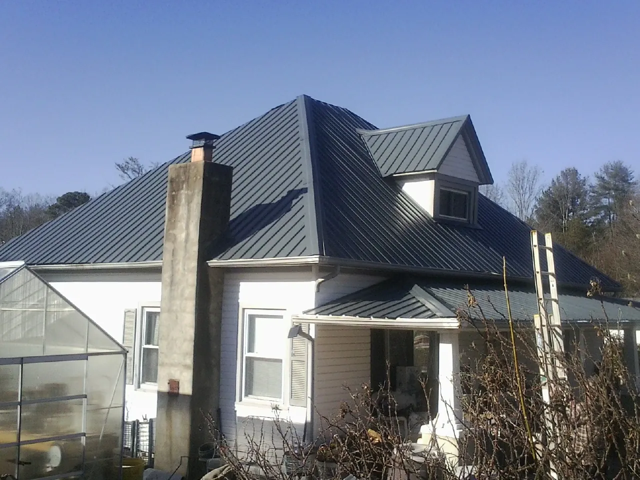 Dark blue standing seam metal roof on a white farmhouse with dormer — Slate & Tile Roof Repair by Roofing Brothers in Cedar Bluffs
