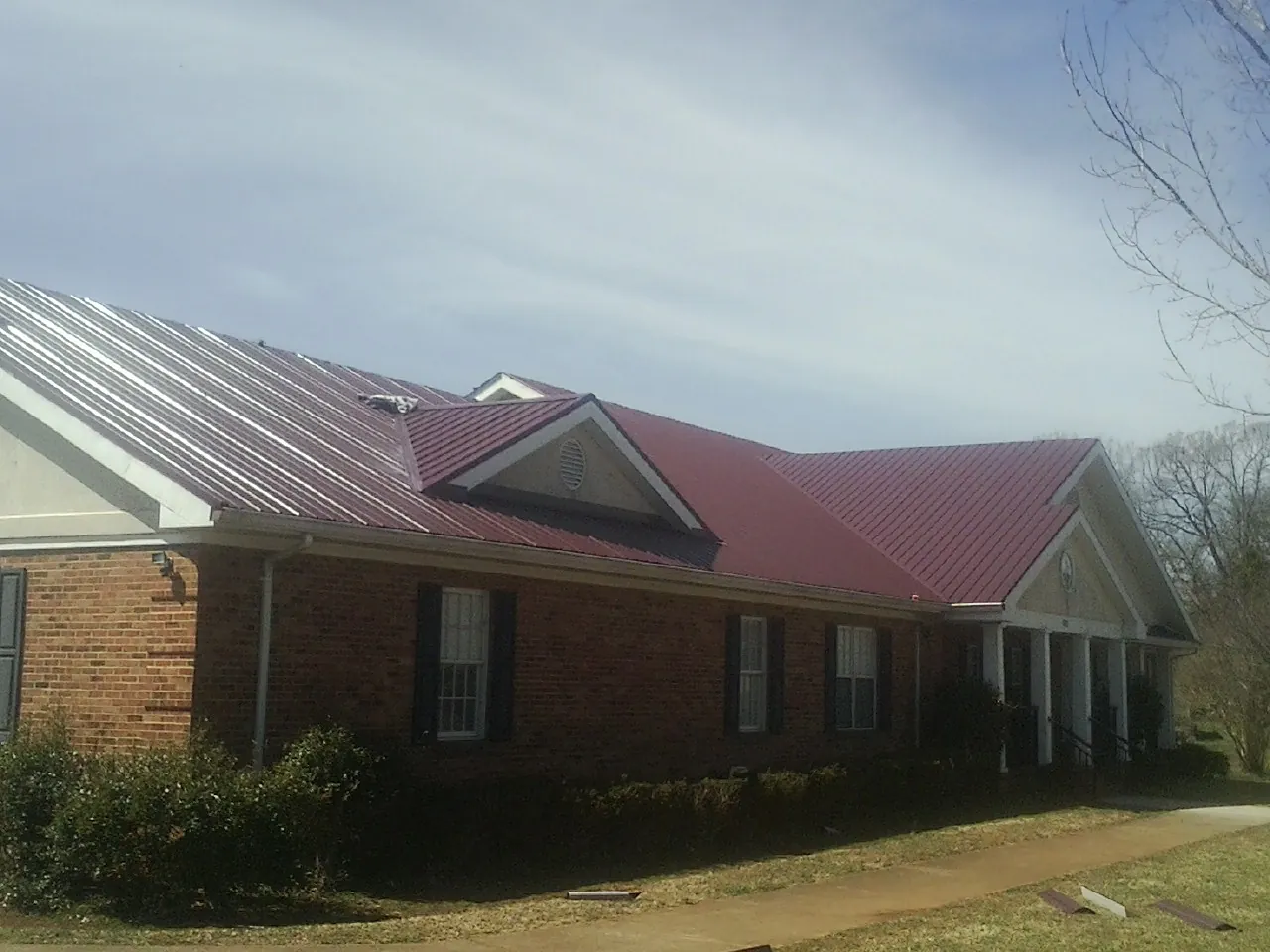 Red metal roof with gabled entries on a long brick building, from a Hail Damage Roof Repair job in Cedar Bluffs