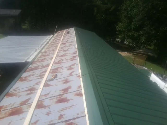 Old rusted panels beside newly installed green metal roofing — Wind Damage Roof Repair by Roofing Brothers in Cedar Bluffs