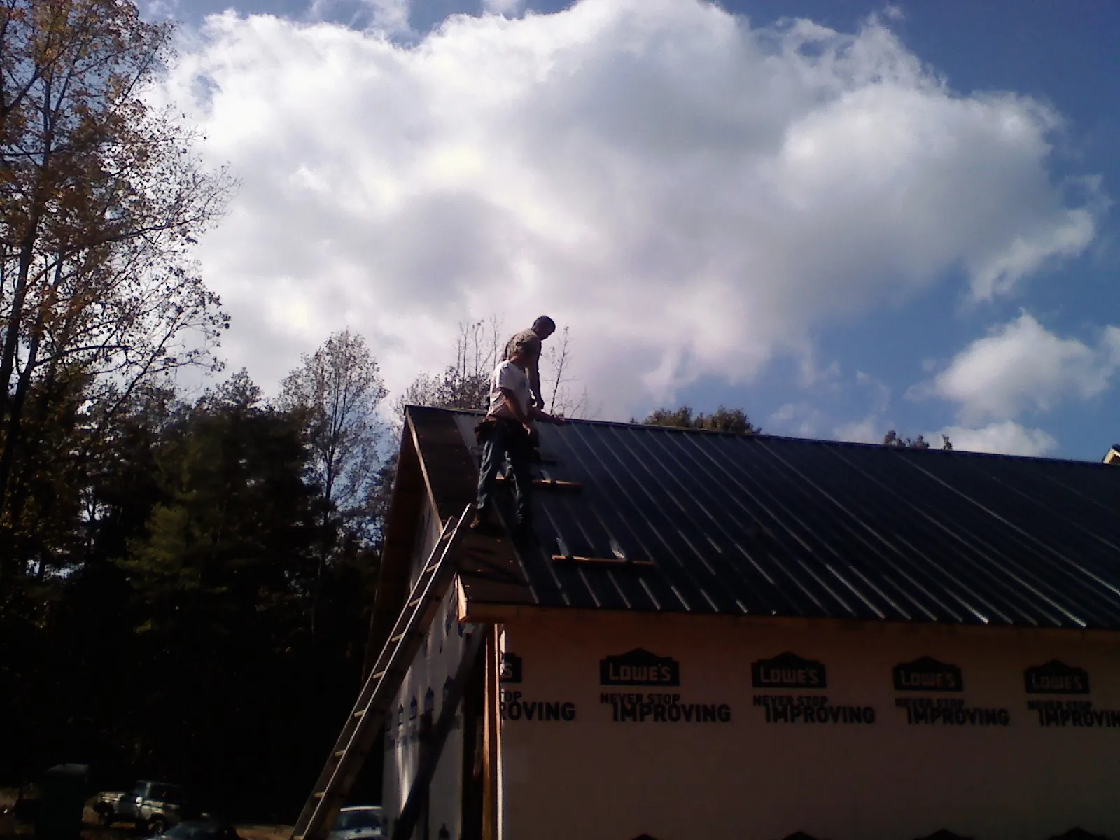 Roofer fastening dark metal panels high against a cloudy sky, from a Roof Inspection job in Cedar Bluffs
