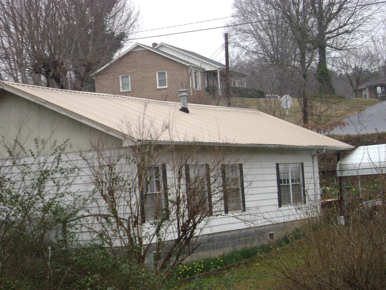 Tan metal roof on a white sided house set into a hillside — Commercial Roofing by Roofing Brothers in Cedar Bluffs