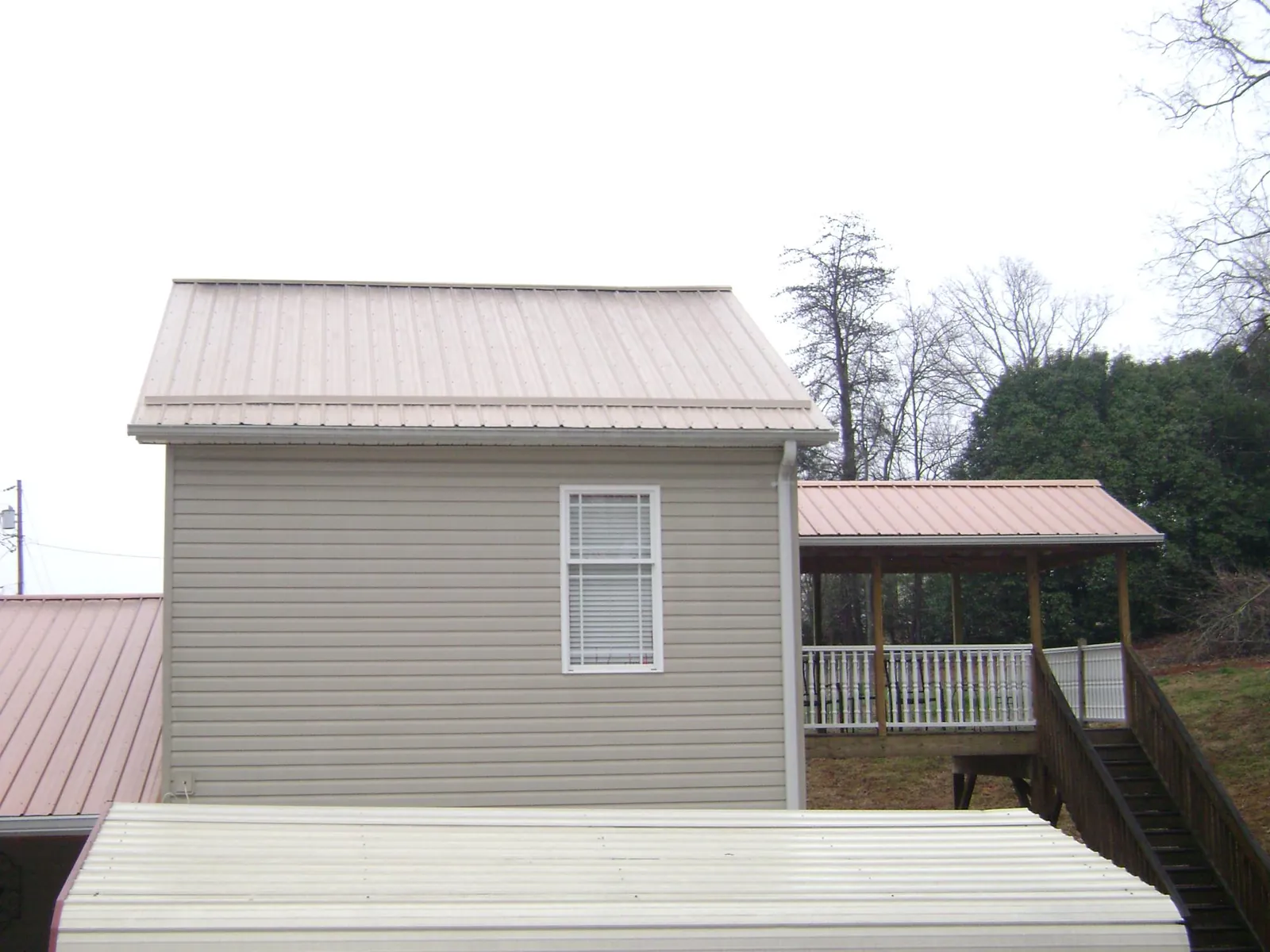 Tan metal roofs on a two story addition and attached porch, from a Roof Replacement job in Cedar Bluffs